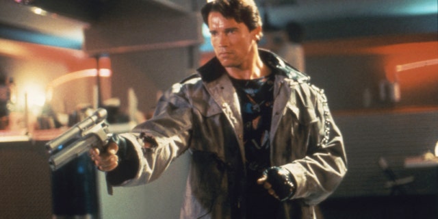 Arnold Schwarzenegger holding a weapon in a scene from "Terminator," where he is wearing a brown leather jacket