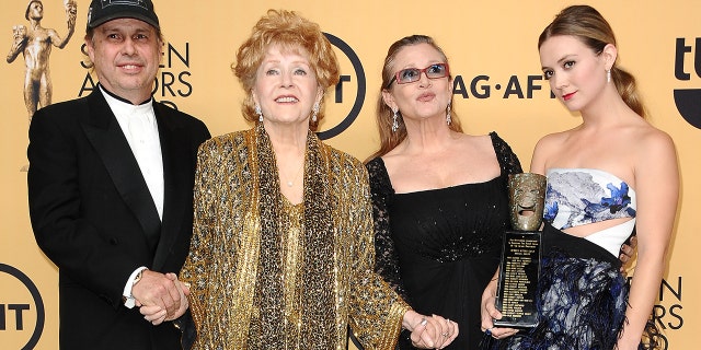 Todd Fisher in a black suit and cap holds mother Debbie Reynold's hand in a gold suit, holding the hand of daughter Carrie Fisher in black, with her daughter Billie Lourd posing in a printed dress with cut-outs holding a SAG Award