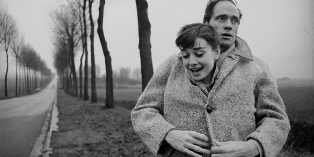 Mel Ferrer envelopes his wife Audrey Hepburn, buttoning her up in his coat, in a picture taken outside Paris in 1956