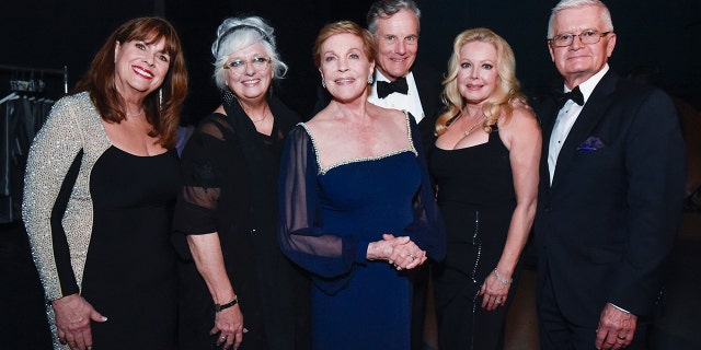 The cast of the sound of music wearing various shades of black and navy posing together for a photo