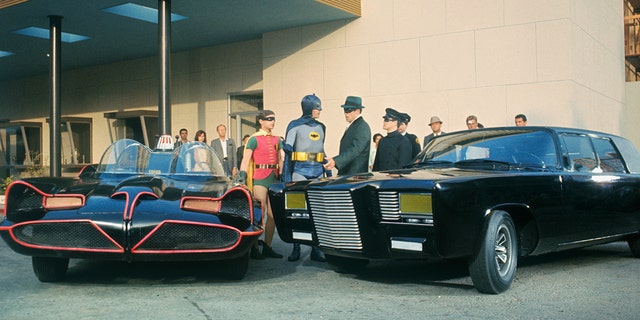The cast of The Green Hornet and Batman in costume next to cars