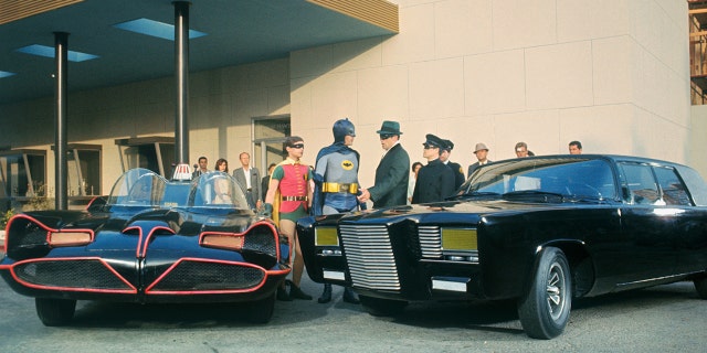 The cast of The Green Hornet and Batman in costume next to cars