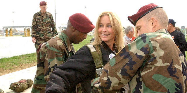 Bo Derek smiling in a black outfit getting suited up