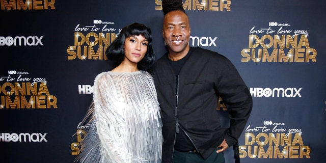 Brooklyn Sudano wearing a silver dress posing next to Roger Ross Williams wearing an all black ensemble