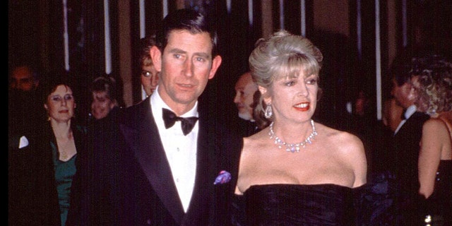 Prince Charles in a suit and bowtie accompanied by Dale Tryon in a low cut black dress with jewels