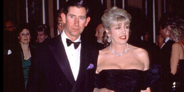 Prince Charles in a suit and bowtie accompanied by Dale Tryon in a low cut black dress with jewels