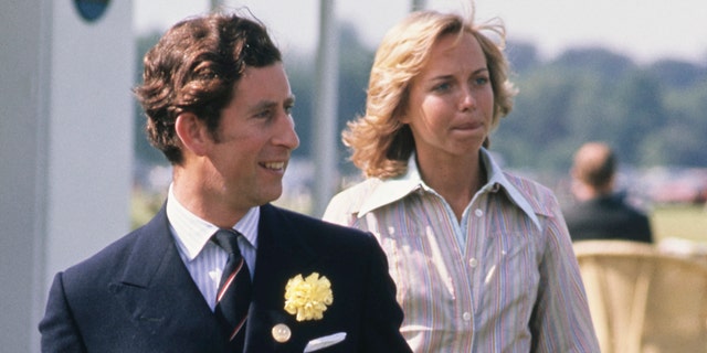 Prince Charles in a dark suit and tie walking in front of Davina Sheffield who is wearing a stripe pastel blouse
