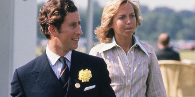 Prince Charles in a dark suit and tie walking in front of Davina Sheffield who is wearing a stripe pastel blouse