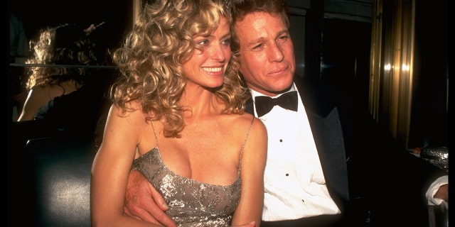 Farrah Fawcett in a sparkly dress cuddling up next to Ryan ONeal in a suit and bowtie