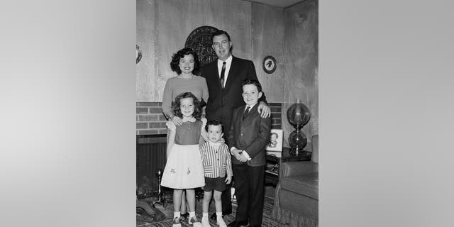 A formal portrait of Jerry Mathers in a suit posing with his family at home during 1960