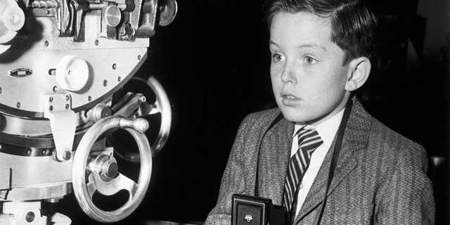 Jerry Mathers holding a camera while wearing a suit