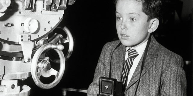 Jerry Mathers holding a camera while wearing a suit