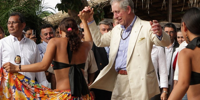 King Charles in a beige blazer and matching pants with a light blue shirt dancing with a woman in the tropics