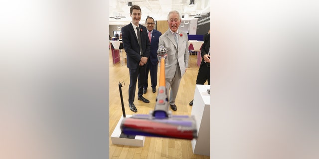 King Charles holding a vacuum cleaner while laughing