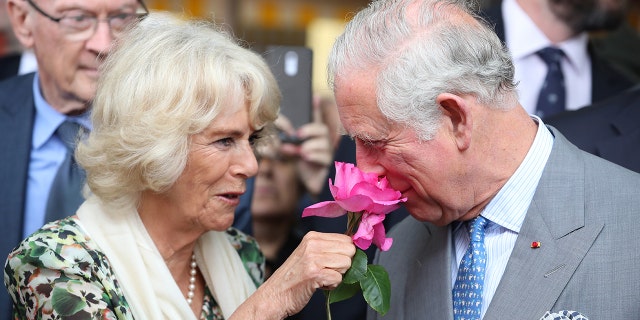 Queen Camilla in a green and white dress holding a pink nose to King Charles nose