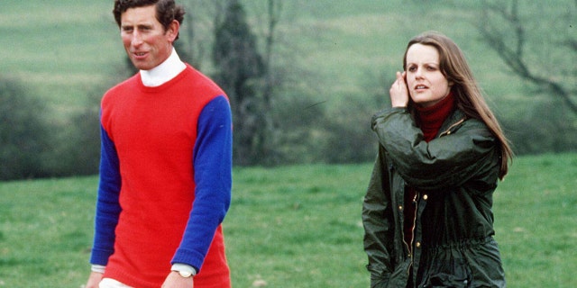 Prince Charles wearing a blue and red sweater walking on a field with Lady Jane in a green coat