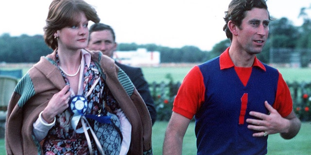 Prince Charles in a blue and red polo shirt walking next to Lady Sarah Spencer in a brightly printed dress