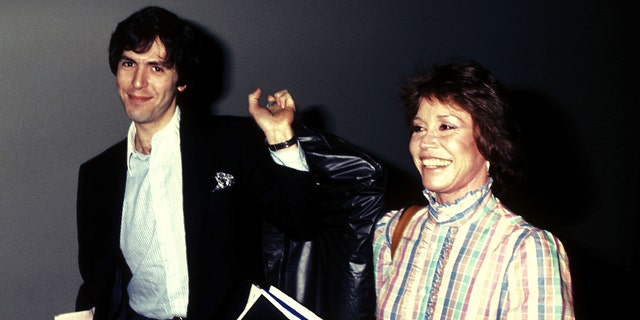 Dr. Robert Levine weairng a black blzer and a white shirt next to Mary Tyler Moore in a plaid dress