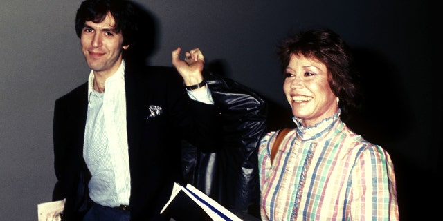 Dr. Robert Levine weairng a black blzer and a white shirt next to Mary Tyler Moore in a plaid dress