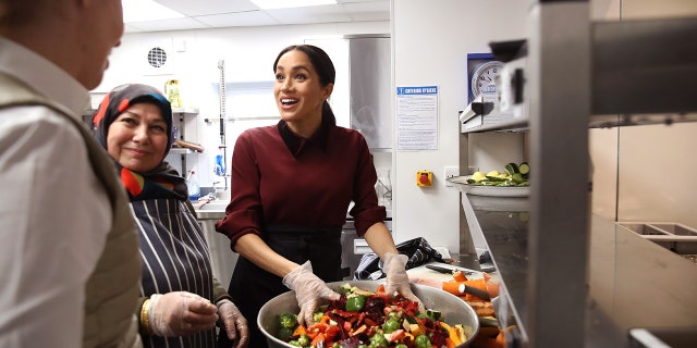 Meghan Markle wearing a burgundy sweater and gloves handling food