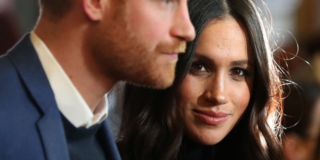 Meghan Markle looking directly at the camera as Prince Harry looks away