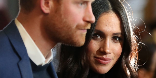 Meghan Markle looking directly at the camera as Prince Harry looks away