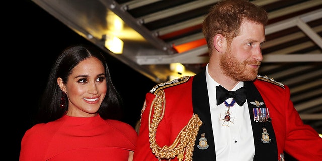 Meghan Markle wearing a red dress walking alongside Prince Harry in a red royal uniform