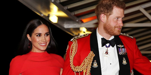 Meghan Markle wearing a red dress walking alongside Prince Harry in a red royal uniform