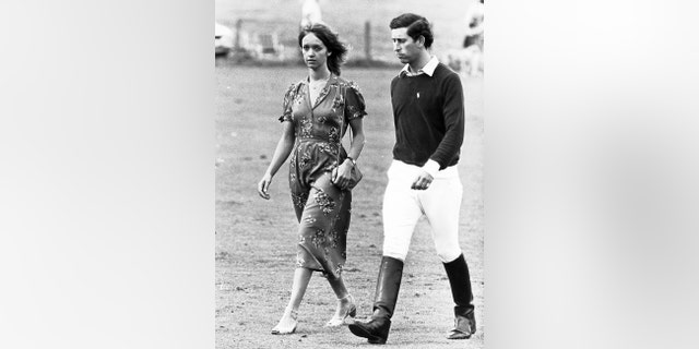 Prince Charles in a polo outfit walking alongside Sabrina Guinness in a printed dress