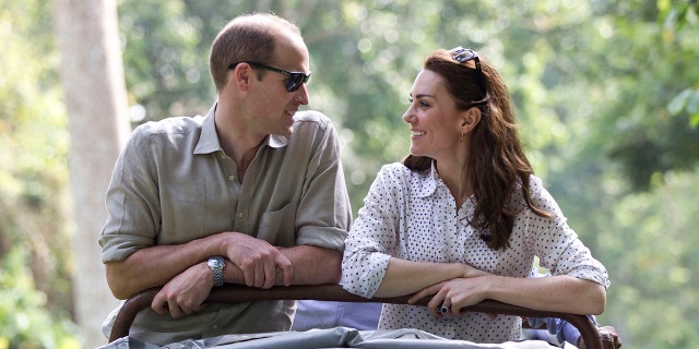 Prince William in a beige shirt and sunglasses looking at Kate Middleton in a white blouise