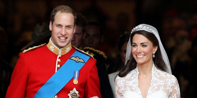 Prince William in a red royal uniform holding the hand of kate middleton wearing a bridal gown