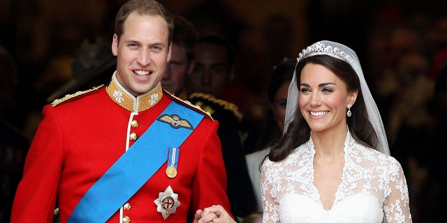 Prince William in a red royal uniform holding the hand of kate middleton wearing a bridal gown