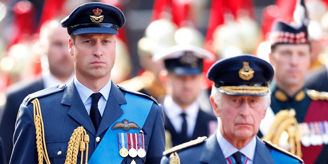 Prince William walking behing his father King Charles as they both wear military suits