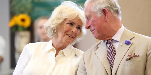 Queen Camilla in a beige blouse looks lovingly at her husband King Charles in a matching suit and tie