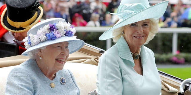 Queen Elizabeth in a blue dress next to Camilla in a lighter blue dress sitting in a royal carriage