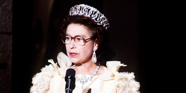 Queen Elizabeth wearing a white dress and glasses giving a speech