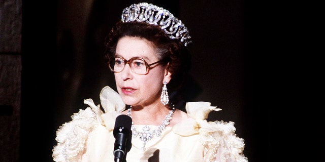 Queen Elizabeth wearing a white dress and glasses giving a speech