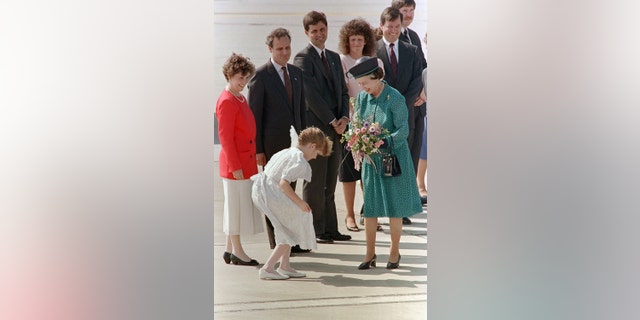 Queen Elizabeth wearing a green dress and holding a bouquet of flowers