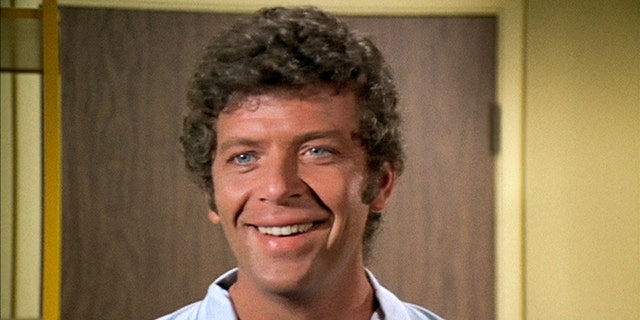 A close-up of Robert Reed wearing a white shirt and smiling as Mike Brady