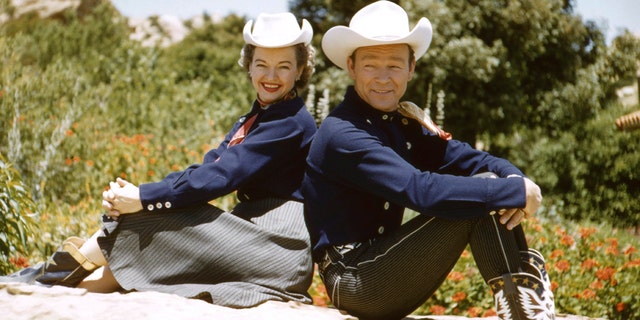 Roy Rogers Dale Evans posing back to back in western clothes.