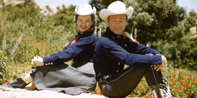 Roy Rogers Dale Evans posing back to back in western clothes.