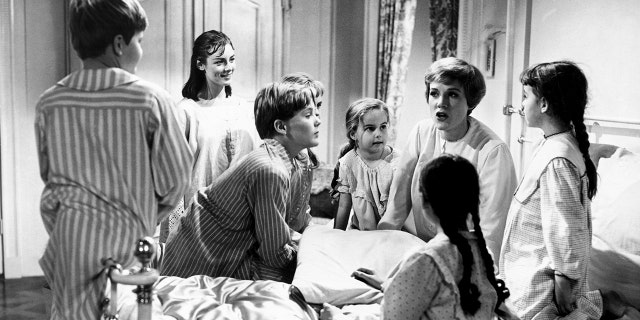 Julie Andrews in bed wearing pajamas telling the von trapp children a story