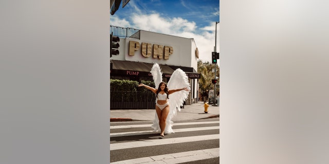 Ella Halikas in white lingerie and angel wings with her arms stretched out