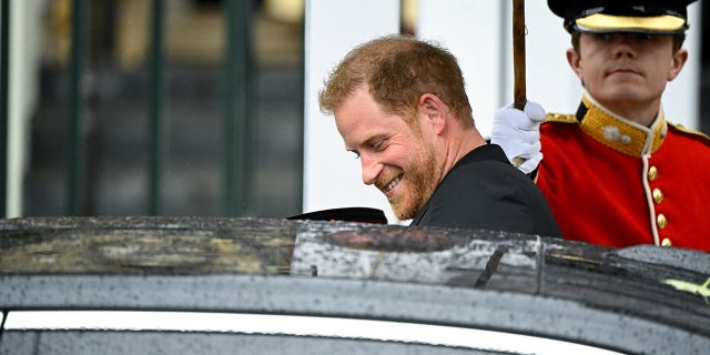 A smiling Prince Harry entering a black car