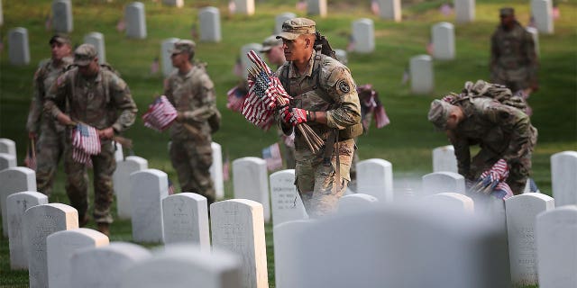 Military members placing flags on tombstones