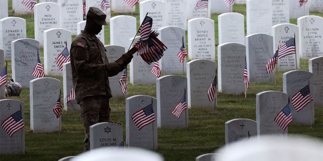A soldier holds a flag and places it on a tombstone.
