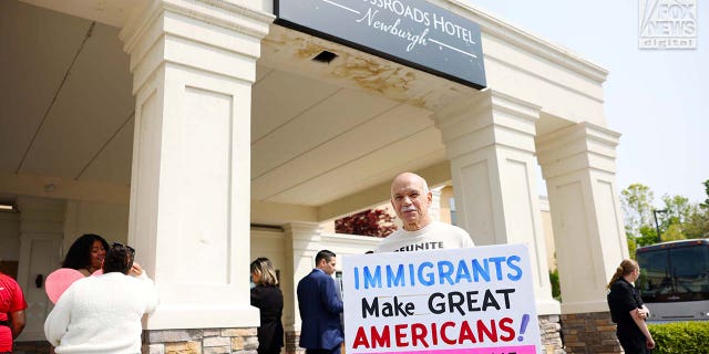 Man holds a hand-painted sign in front of the hotel