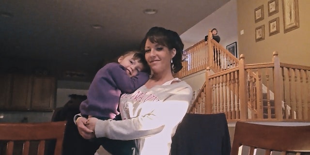 Judy Malinowski, wearing a white sweater while carrying her daughter