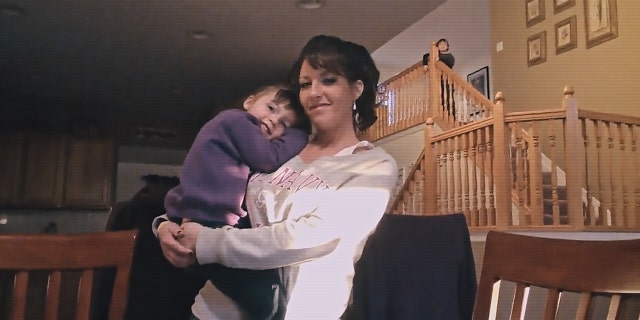 Judy Malinowski, wearing a white sweater while carrying her daughter