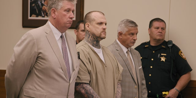 Michael Siager standing up in a beige jumpsuit during trial